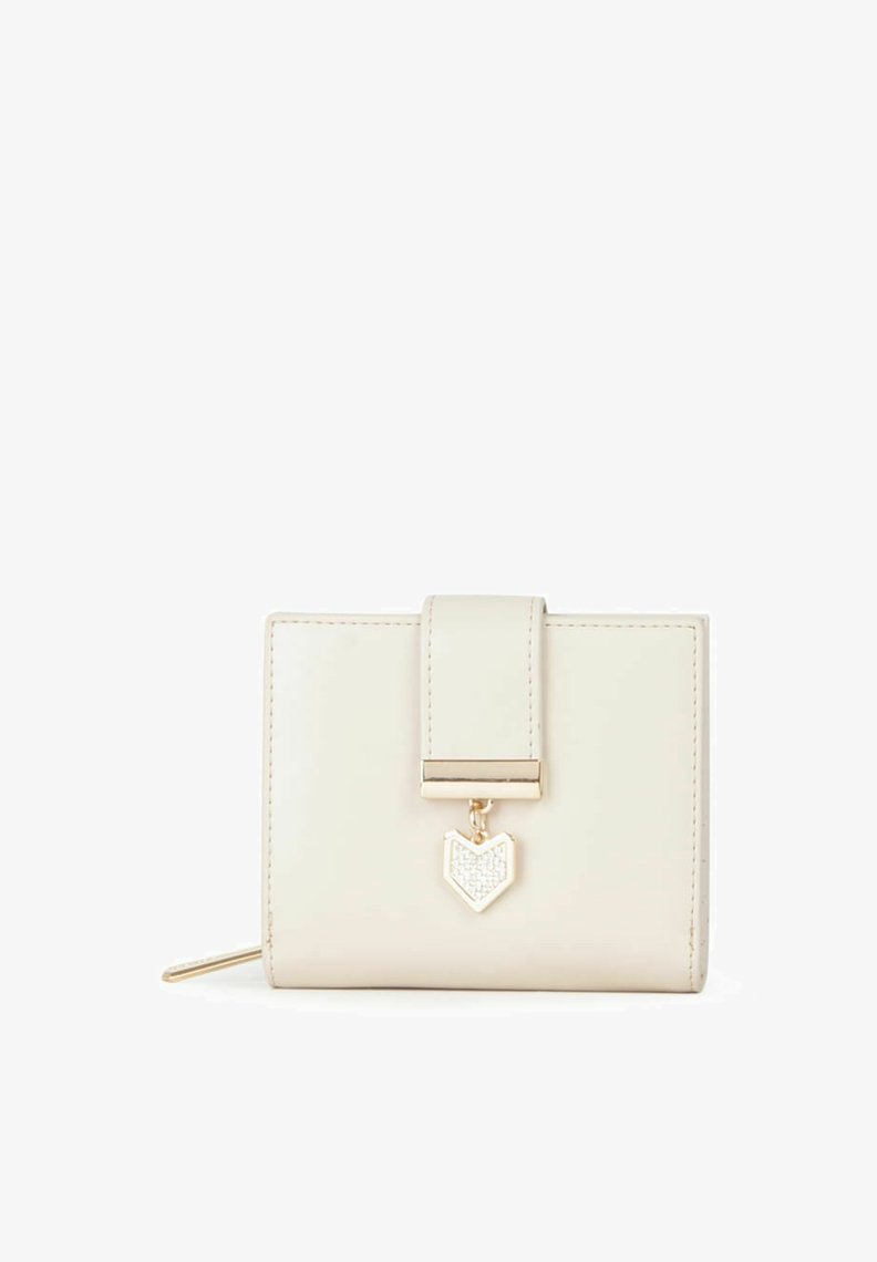 Cartera de cuero crema con herrajes dorados, cierre de solapa y un charm en forma de corazón con un detalle brillante. Forma cuadrada compacta.