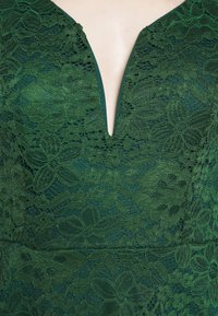 Tissu en dentelle vert foncé avec des motifs floraux et un col en V sur un vêtement.