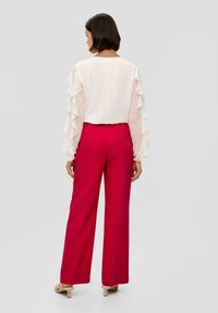 Witte blouse met ruches aan de mouwen, gecombineerd met hoog-zitende rode wijde broek. Model draagt beige hakken, en laat een stijlvolle achterkant zien.