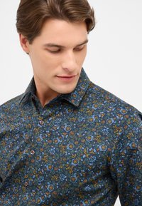 Bloemendesshirt in donkerblauw, met groene, gele en oranje accenten. De stof heeft een soepele textuur met een gestructureerde kraag.