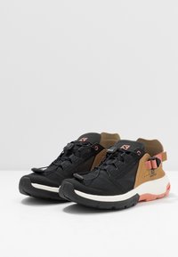 Scarpe sportive nere e marroni con tomaia in rete, linguetta, lacci regolabili e suola intermedia bianca con accenti arancioni.