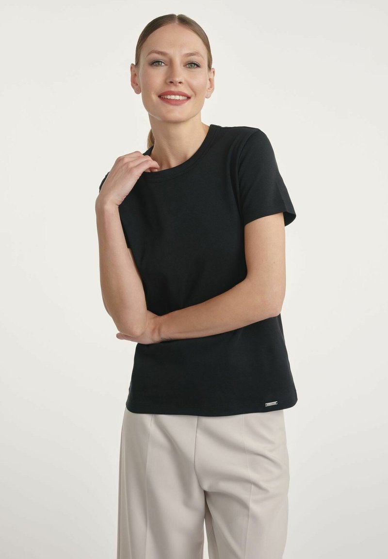 Czarna bawełniana koszulka z okrągłym dekoltem i krótkimi rękawami, z subtelną metką marki u dołu, w połączeniu z jasnymi spodniami.