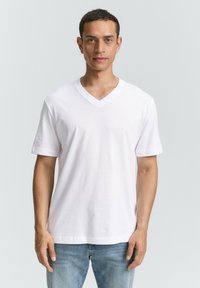 Weißes Baumwoll-V-Ausschnitt-T-Shirt mit kurzen Ärmeln, das einen lässigen Schnitt und eine glatte Textur aufweist. Getragen mit hellblauen Jeans.