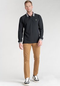 Zwart polo shirt met lange mouwen en een witte gestreepte kraag; gecombineerd met tan kleuren broeken en zwart-witte sneakers; aansluitend ontwerp, gemaakt van katoen.