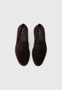 Brown suede loafers featuring a rounded toe, penny strap detail, and contrasting stitching. Smooth leather lining and rubber sole.