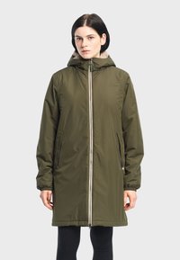 Olivengrøn parka med lynlås foran, hætte og blød, lysebrun falsk pelsforing. Har to sidelommer og elastiske ærmer.