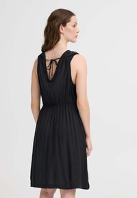 Rochie neagră fără mâneci, cu un nod la spate, talie elastică și fustă fluidă. Fabricată dintr-un material ușor, cu textură textilă ribbed.