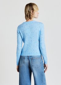 Pull en maille bleu clair avec un motif chiné, col rond et ourlet côtelé ajusté, associé à un jean en denim taille haute.