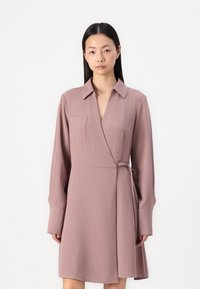 Abito a maniche lunghe avvolgente in rosa polveroso, realizzato in tessuto testurizzato. Presenta un colletto, una cintura laterale e una tasca applicata sul lato sinistro del petto.