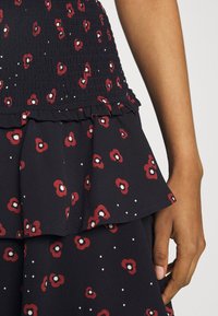 Květinové černé šaty s červeným a bílým vzorem. Mají smockovaný korzet a vrstvený volánkový lem. Vyrobeno z lehké, strukturované látky.