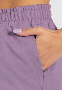 Pantaloni con elastico viola in vita, dotati di una tasca laterale, caratterizzati da una texture liscia e un design aderente, con dettagli di cucitura senza soluzione di continuità.