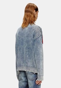 Denim sweater in vervaagd blauw met ribbenmanchetten en -zoom, met rafelige randen en een relaxte pasvorm. Achteraan is er minimale detaillering te zien.