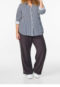 Chemise à rayures bleu marine et blanche avec les manches retroussées, associée à un pantalon ample gris foncé et des baskets blanches.