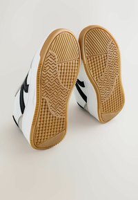 Baltos sportbačiai su juodais akcentais, tekstūruotais gumos pado ir raštuotu sukibimu. Dizainas turi suapvalintą noselę ir minkštą apykaklę.