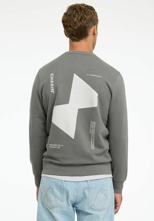 Grå sweatshirt med texturerad tyg, en stor vit geometrisk design på ryggen och tryckta textdetaljer. Rund halsringning och ribbade muddarna.