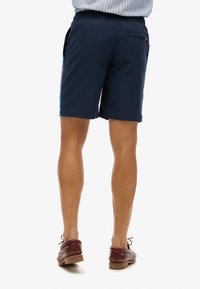 Shorts bleu marine avec taille élastique et poches latérales. Présente une bande de couleur contrastante sur les côtés et une poche arrière.