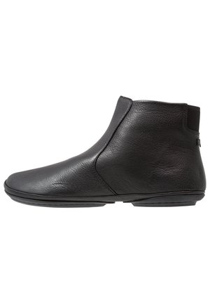 Bottes noires en cuir à la cheville avec une forme élégante, une texture lisse, des panneaux latéraux élastiques et une semelle en caoutchouc plate. Détails minimaux sur le dessus.