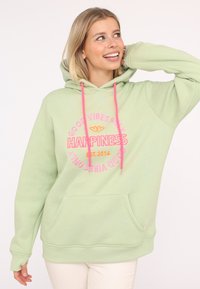 Hoodie vert clair avec une poche avant, cordons de serrage roses et texte brodé : "SEULEMENT DES BONNES VIBRATIONS" et "BONHEUR ÉTABLI EN 2014". Texture douce.