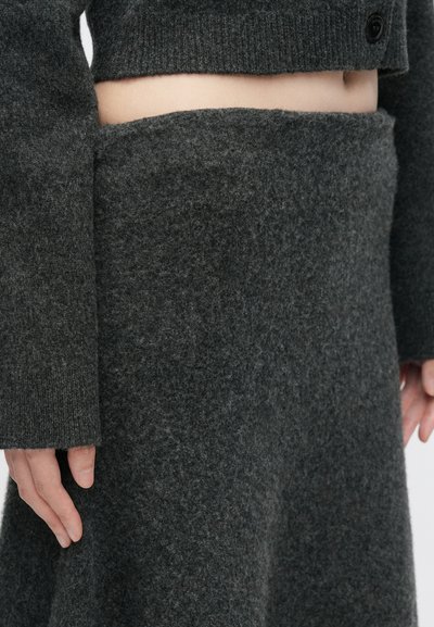 Γκρι μάλλινο πουλόβερ με φαρδιές μανίκες και cropped σχέδιο, συνδυασμένο με μια αντίστοιχη ψηλόμεση φούστα φτιαγμένη από το ίδιο υφαντό υλικό.