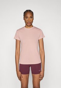 Šviesiai rožinė sportinė marškinėliai trumpomis rankovėmis, apvalia iškirpte ir lygiu paviršiumi. Derinami su bordo šortais, kuriuose yra kontrastingas logotipo detalė.