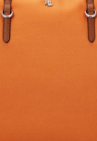Narancssárga textil táska barna bőr kiegészítőkkel. Ezüst színű hardverrel és középen dombornyomott logóval rendelkezik. Strukturált felület.