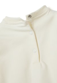 Close-up van een roomkleurige ribbelkraag met drie witte drukknoopjes op een zacht stoffen kledingstuk.