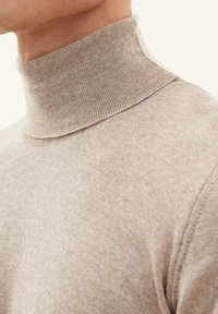 Beige strikket turtleneck sweater med slim fit og ribbet krave. Texturen er glat med subtile farvevariationer.
