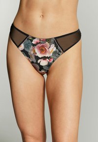 Ziedu raksta bikini apakšbikses ar melnu fonu, piedāvā mežģīņu sānus, viļņainas malas un mīkstu auduma tekstūru.