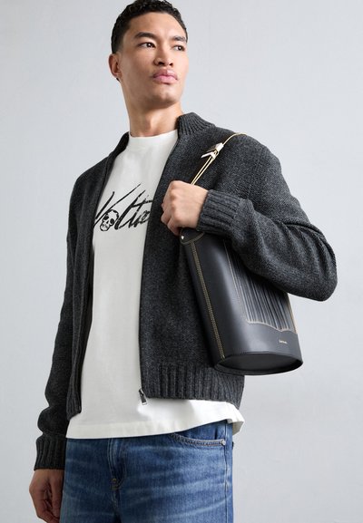Cardigan en tricot gris foncé avec un col haut, porté sur un t-shirt blanc avec un graphique noir, associé à un sac à main texturé noir.