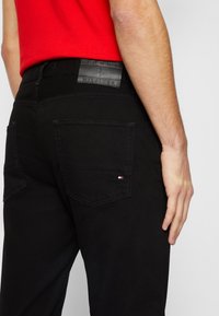 Jeans de mezclilla negra con una textura suave, que cuentan con dos bolsillos traseros y una etiqueta de piel negra de marca en la cinturilla.