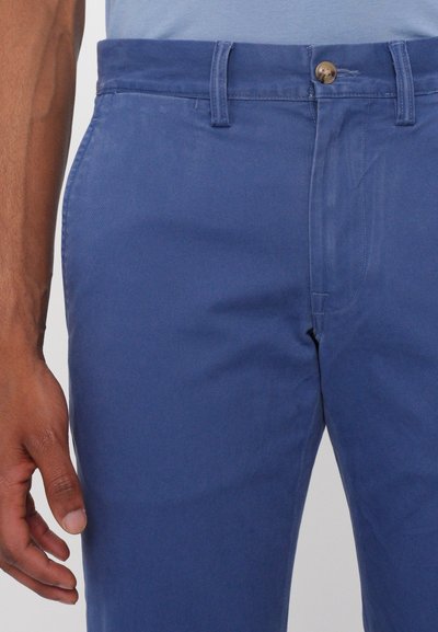 Chinos in cotone blu con una texture liscia, dotati di chiusura con bottone frontale, passanti per cintura e tasche laterali.
