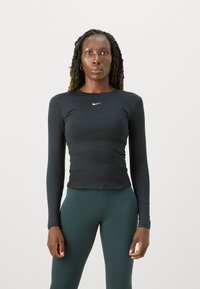 Svart langermet treningstopp laget av elastisk stoff, med rund hals og en liten hvit Nike-logo på brystet.