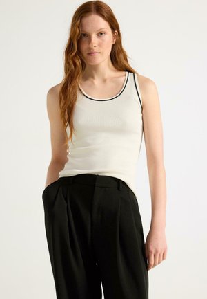Top a righe bianco con bordatura nera, abbinato a pantaloni neri con vita alta e pieghe, caratterizzati da una texture liscia e un fit rilassato.