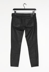 Pantalones de mezclilla negros con corte ajustado. Con dos bolsillos traseros y una textura suave, colgando de una percha negra sobre un fondo blanco.