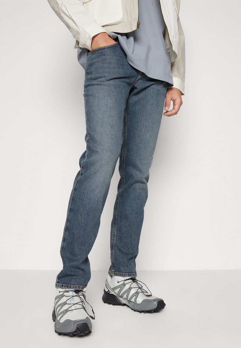Blauwe spijkerbroeken met een rechte snit, gecombineerd met grijze en witte sneakers met zwarte accenten en gestructureerde overlays.