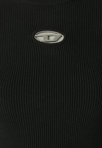 Top preto canelado com um detalhe de logotipo metálico circular na gola, apresentando um tecido texturizado que oferece uma silhueta ajustada.