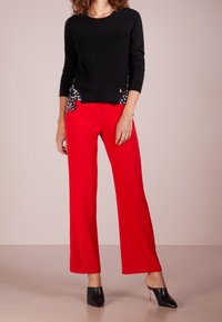 Czarny sweter z długim rękawem o wzorzystym wykończeniu, w zestawieniu z czerwonymi spodniami o szerokich nogawkach oraz czarnymi szpilkami. Gładka faktura, elegancki design.