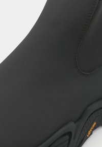 Black waterproof boot with a smooth upper surface and a textured sole, displaying the Vibram logo in orange.