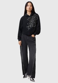 Felpa corta nera con design a stampa leopardata e dettagli in borchie argento, abbinata a jeans neri a gamba larga e stivali metallici con tacco alto.