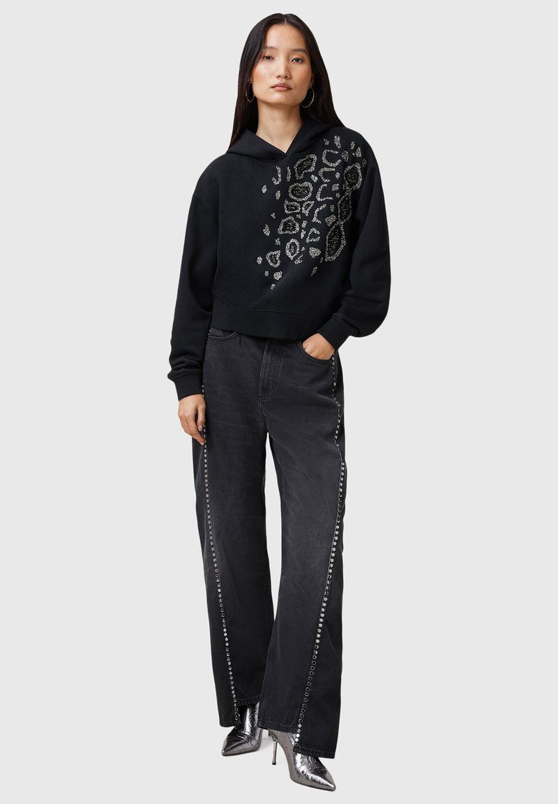 Schwarze, verkürzte Kapuzenjacke mit einem Leopardenmuster und silbernen Nietenakzenten, kombiniert mit schwarzen weit geschnittenen Jeans und metallischen High-Heel-Stiefeln.