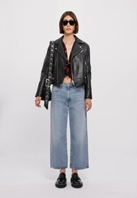 Giubbotto in pelle nera da motociclista su top a fiori crop, abbinato a jeans chiari a gamba larga e scarpe chunky nere. Gli occhiali da sole neri completano il look.
