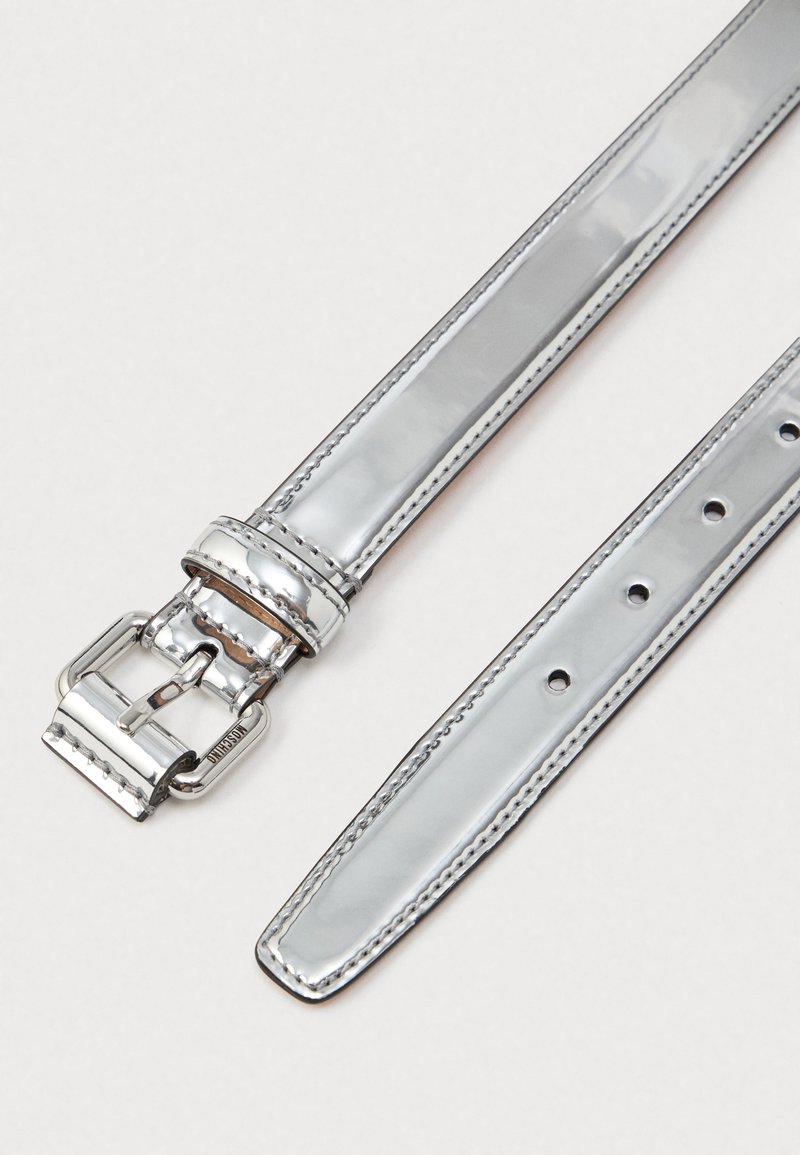 Silverfärgad metallbälte med slät yta, blank finish, har ett metallspänne och flera justeringshål, sydda detaljer längs kanterna.