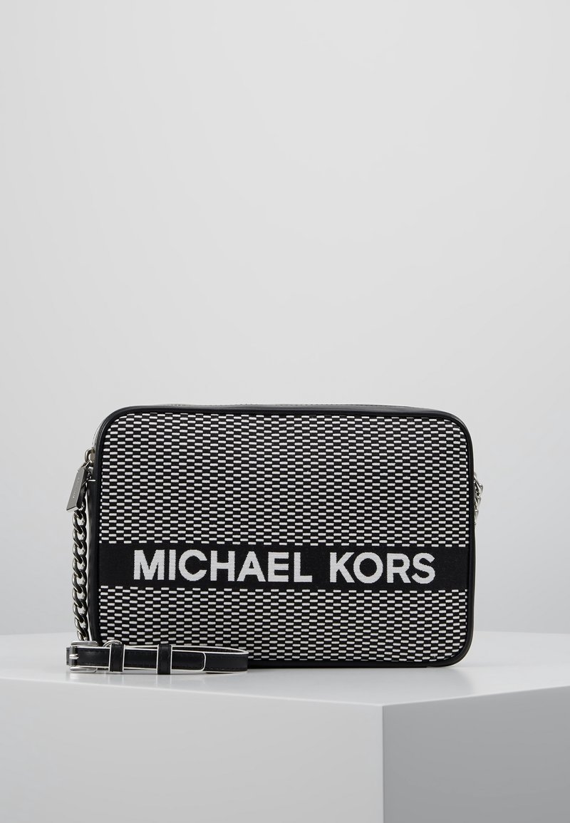 Svart och vitt vävt tyg crossbody-väska med silverkedjesträng. Framsidan visar "MICHAEL KORS" tydligt på en svart rektangulär panel.