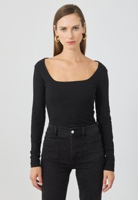 Schwarzes geripptes Langarmoberteil mit quadratischem Ausschnitt, kombiniert mit hochgeschnittenen schwarzen Jeans aus Denim mit Fronttaschen und einer subtilen Textur.