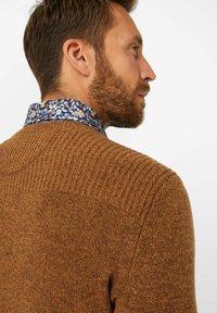 Brauner gestrickter Pullover mit gerippter Textur an den Schultern. Mit einem blauen, floral gemusterten Kragen, der am Hals sichtbar ist.