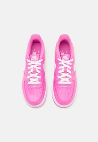Vaaleanpunaiset Nike Air -lenkkarit valkoisilla pohjilla ja nauhoilla. Sileä synteettinen päällinen, rei'itetty varvasosa ja logo kielekkeessä.