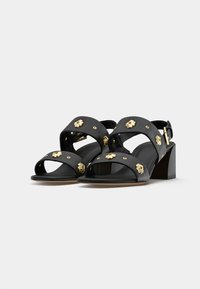 Black leather sandals with gold floral accents, featuring two wide cross straps, an open toe, and a rectangular block heel.