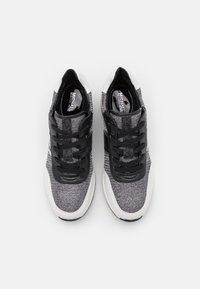 Sneaker sportive a maglia nera e grigia con un upper testurizzato, lacci neri e suole bianche con una finitura liscia.