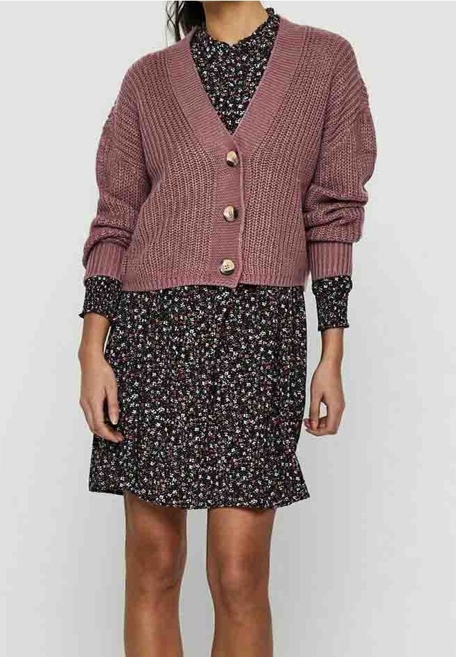 Cardigan en maille mauve, avec un col en V, des manches longues et des boutons en bois. Associé à une robe noire à motifs floraux avec un ourlet volanté.