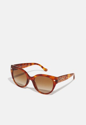 Lunettes de soleil en écaille de tortue marron avec de grandes montures carrées, des verres dégradés et des accents décoratifs sur les branches.